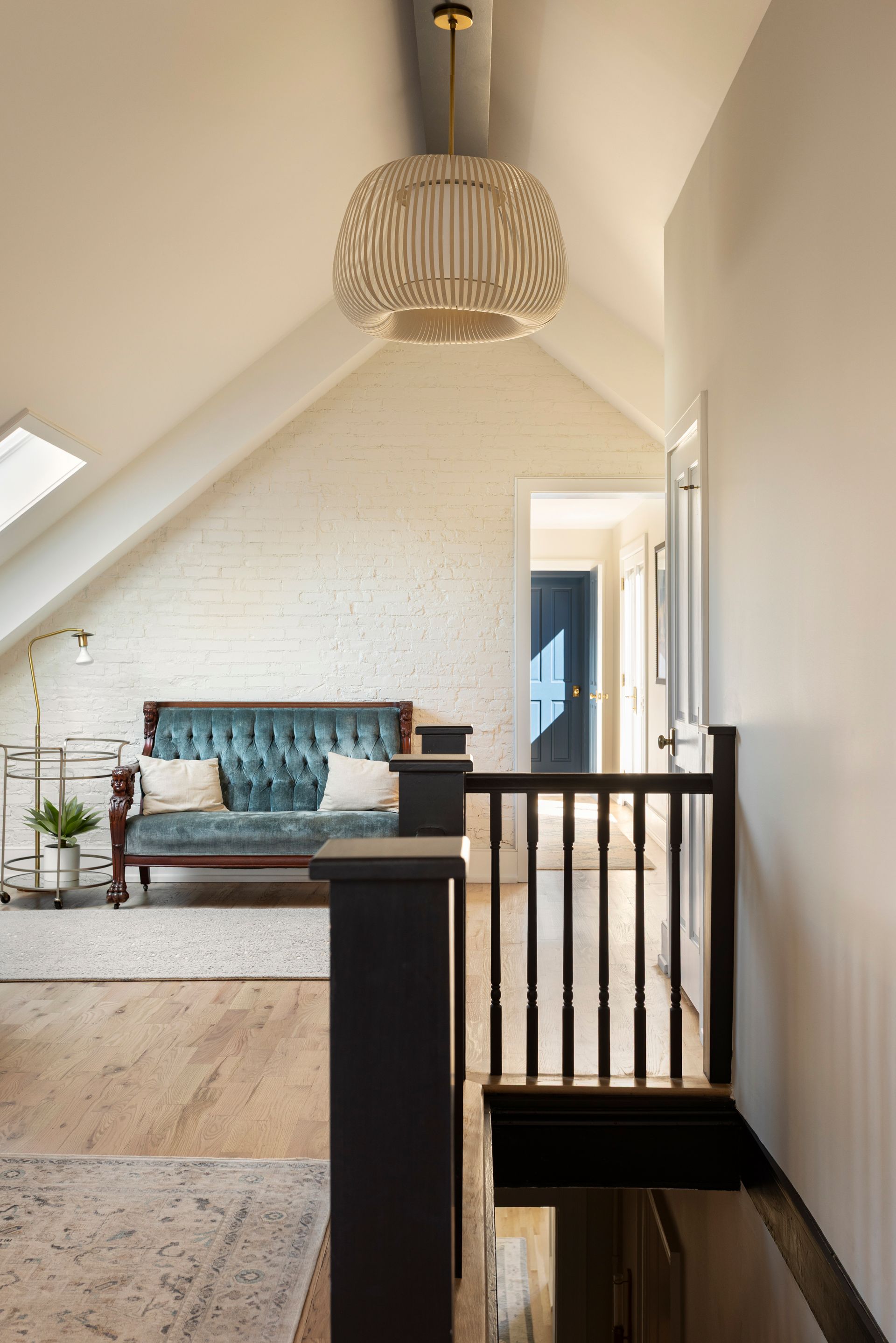 Upstairs landing with whitewashed brick, a skylight and a dark stained stair rail after a whole-house renovation