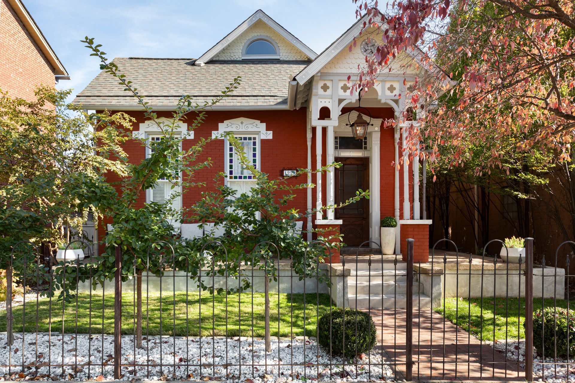 Restored red brick Victorian cottage with white gingerbread porch trim and a stained glass window