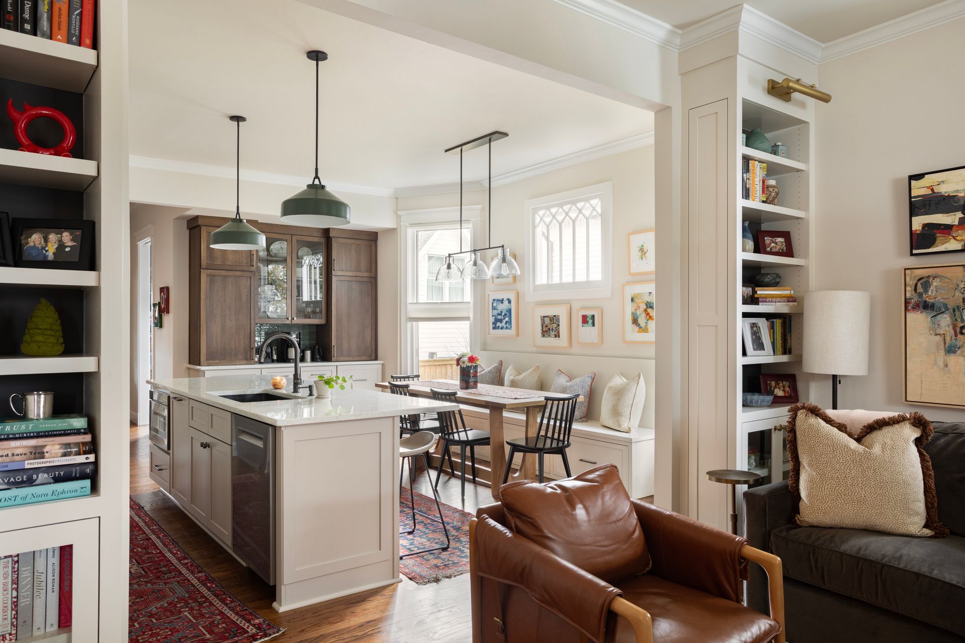 Open kitchen with a stone island, dark timber cabinetry, built-in shelving and a dining banquette beyond