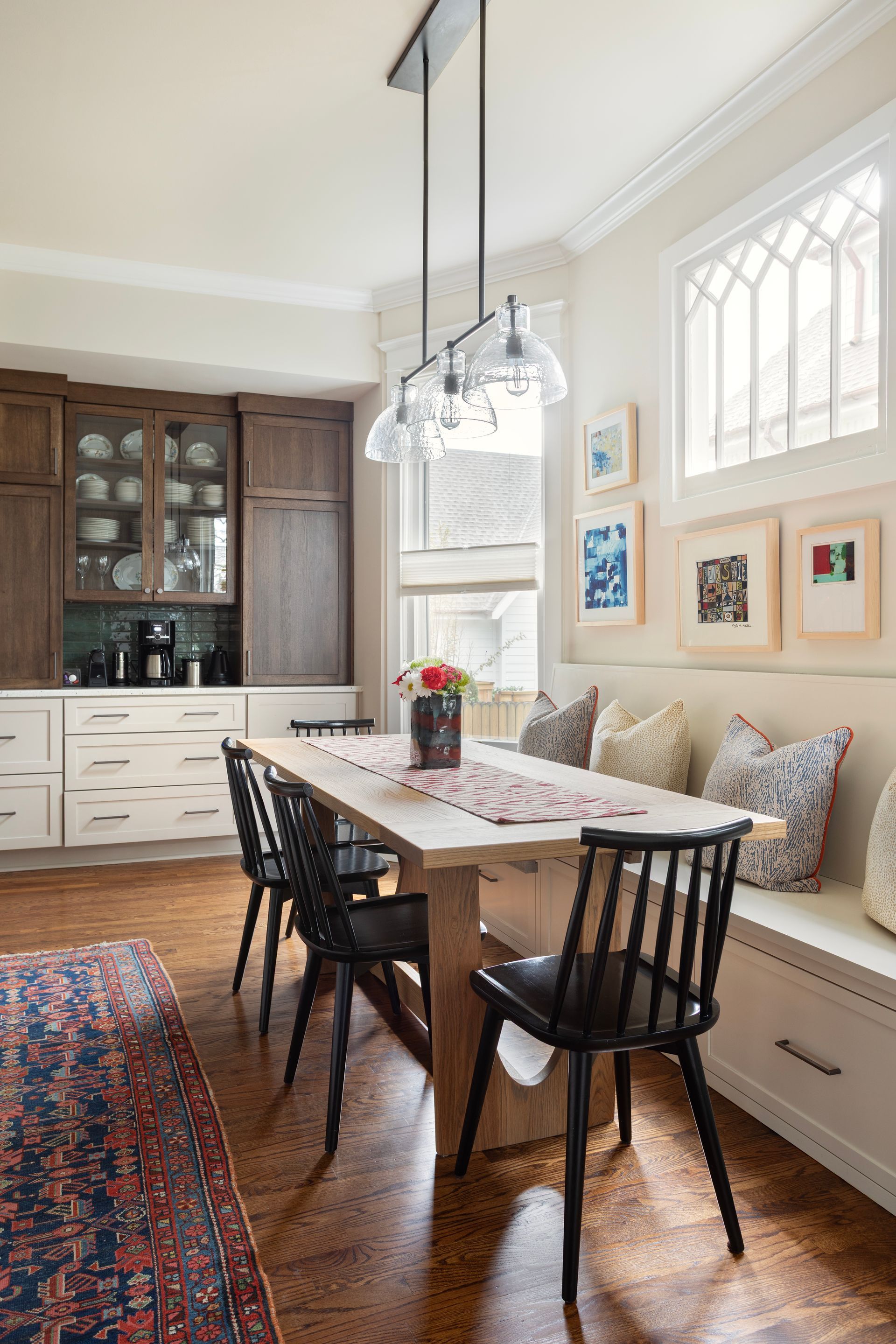 Kitchen dining area with a walnut hutch, built-in banquette seating and glass pendants