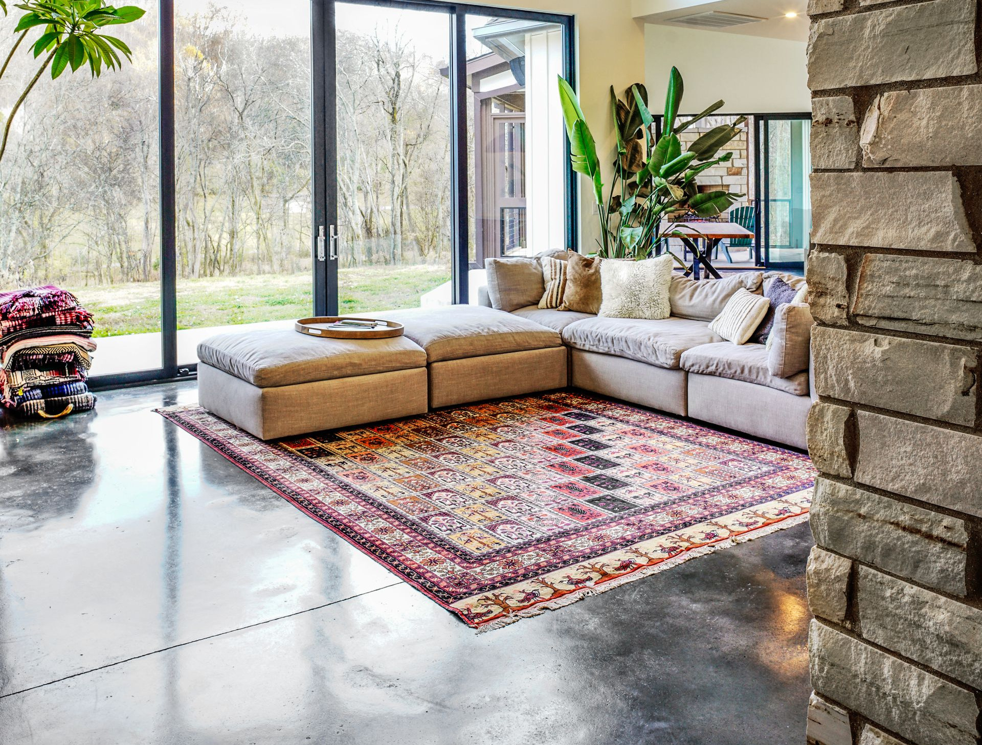 Living room with polished concrete floors, a rough stone wall and floor-to-ceiling glazing onto woodland