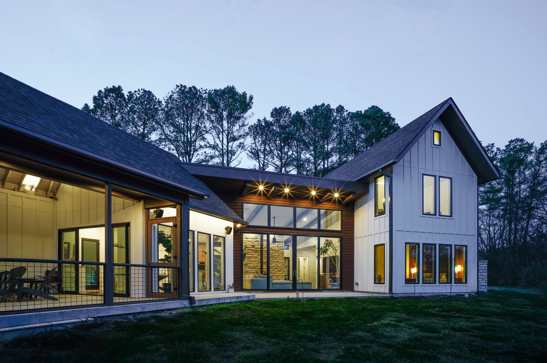 Board-and-batten house at dusk with lit windows, a standing-seam metal roof and a covered porch