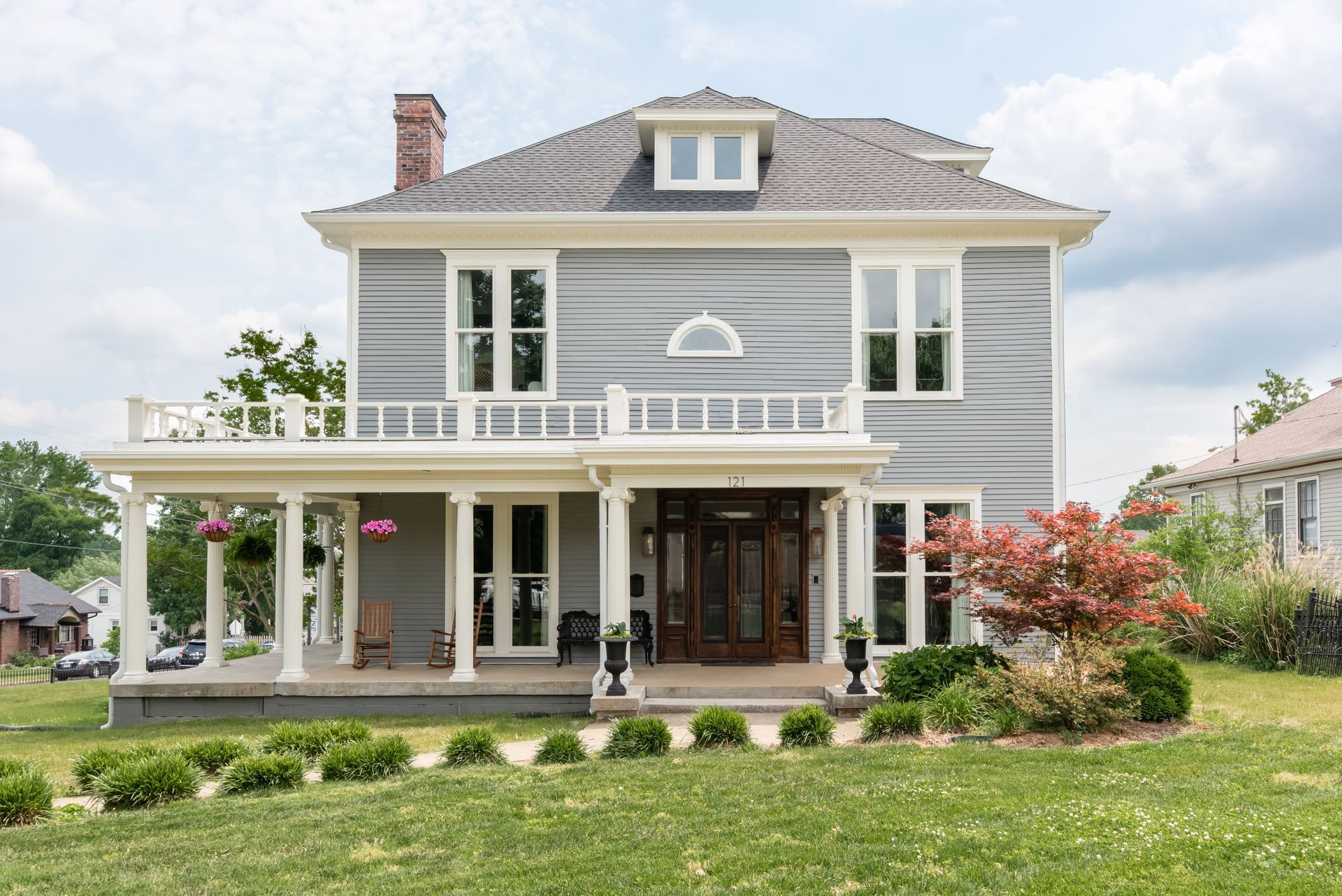 Grey clapboard American foursquare house with a columned wraparound porch and a Japanese maple in the garden