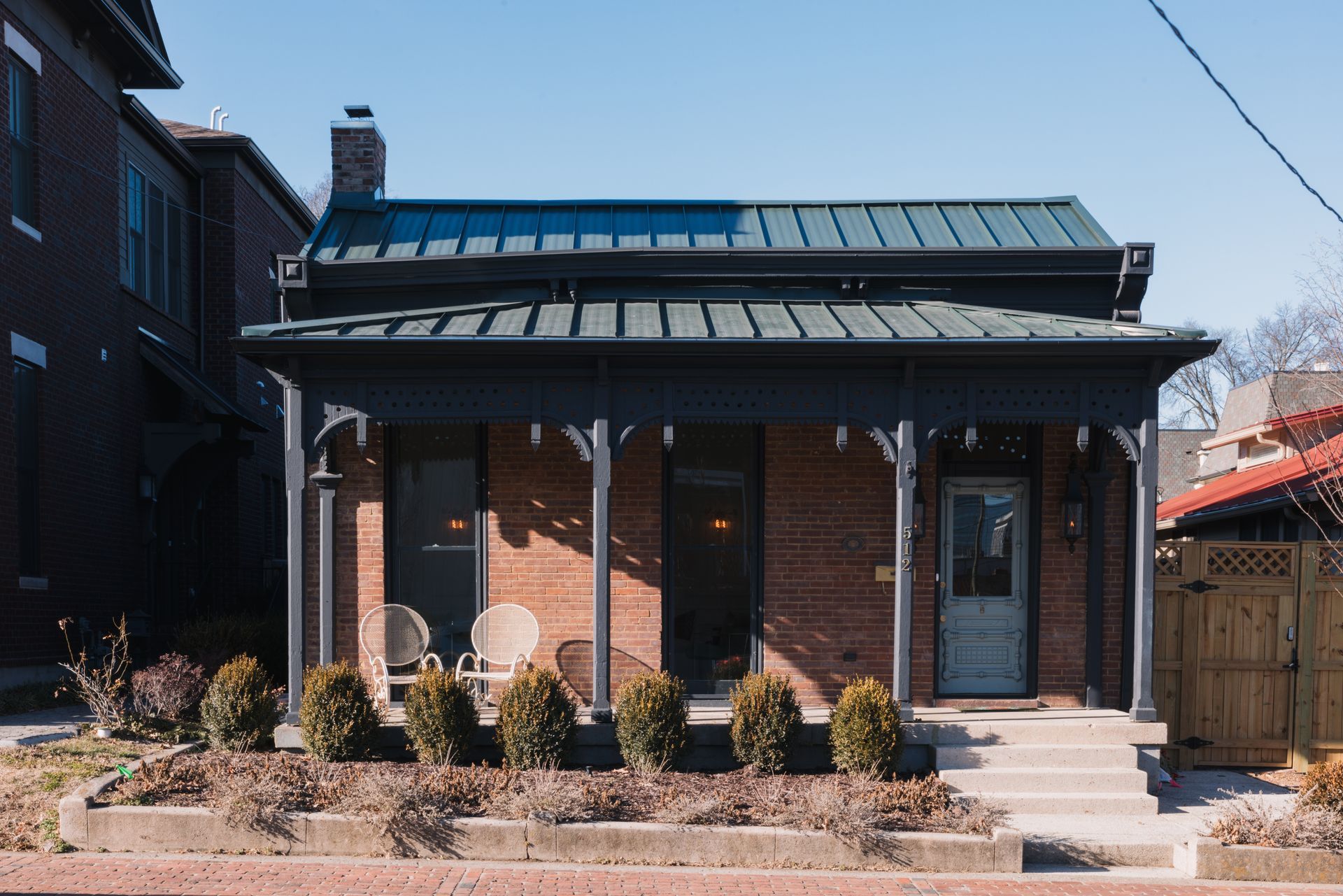Restored brick Victorian cottage with a green standing-seam roof and decorative porch trim
