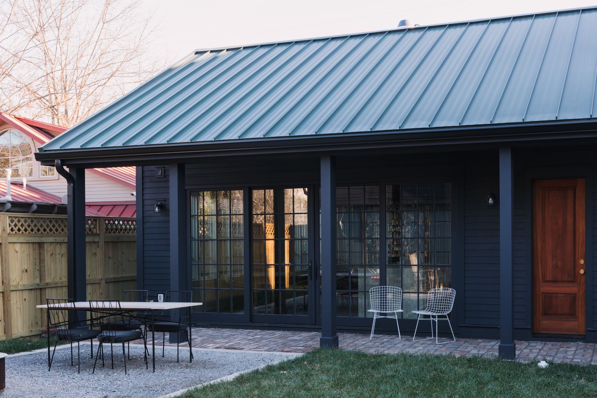 Detached dwelling clad in dark siding with a green standing-seam roof, glazed doors and a brick patio