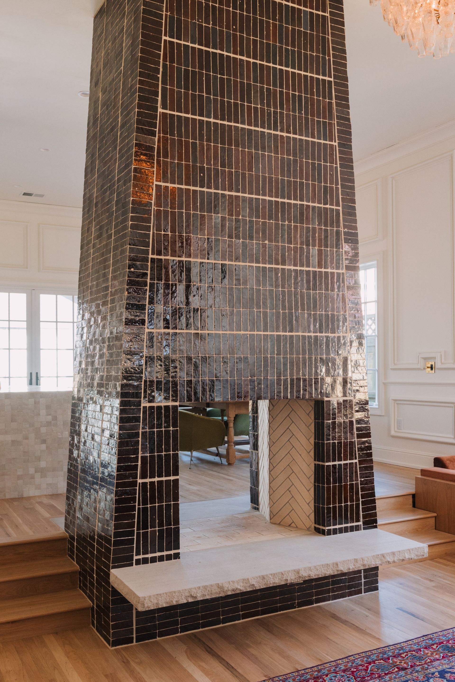 Double-sided fireplace clad in dark glazed tile with a rough-cut stone hearth