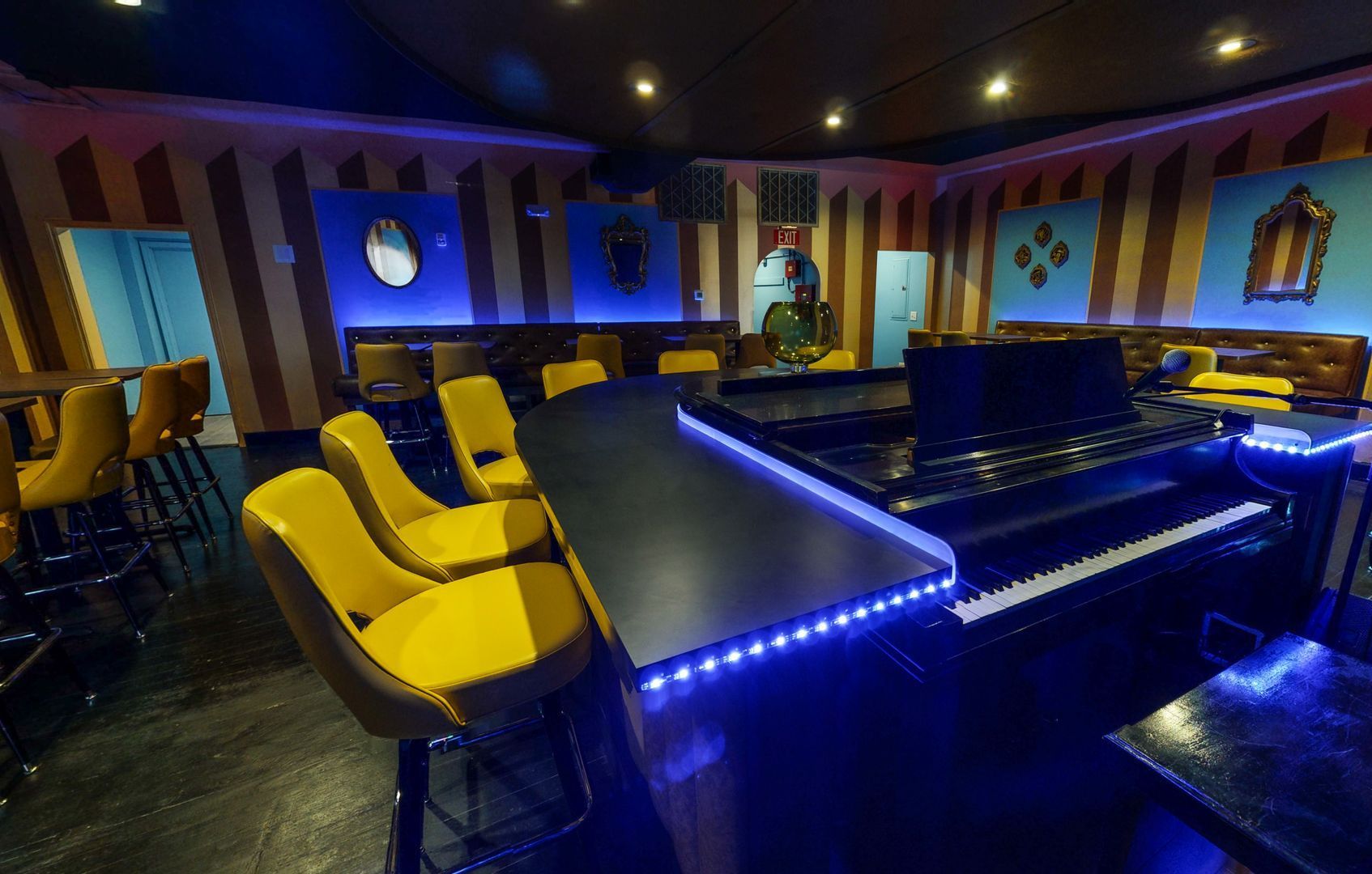 Piano bar interior with a curved counter, yellow leather stools and striped painted walls