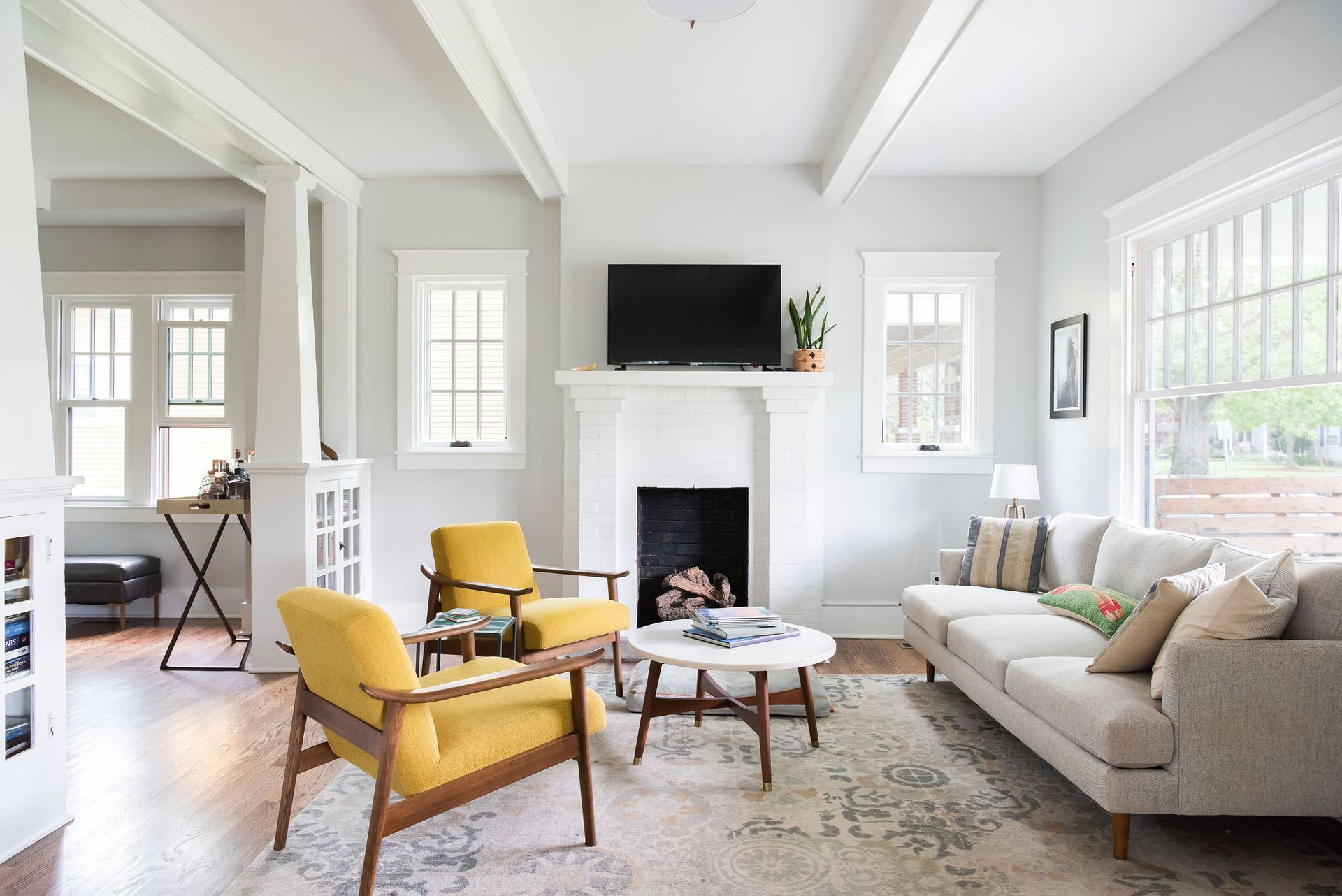 Bright craftsman living room with a white painted brick fireplace and exposed ceiling beams