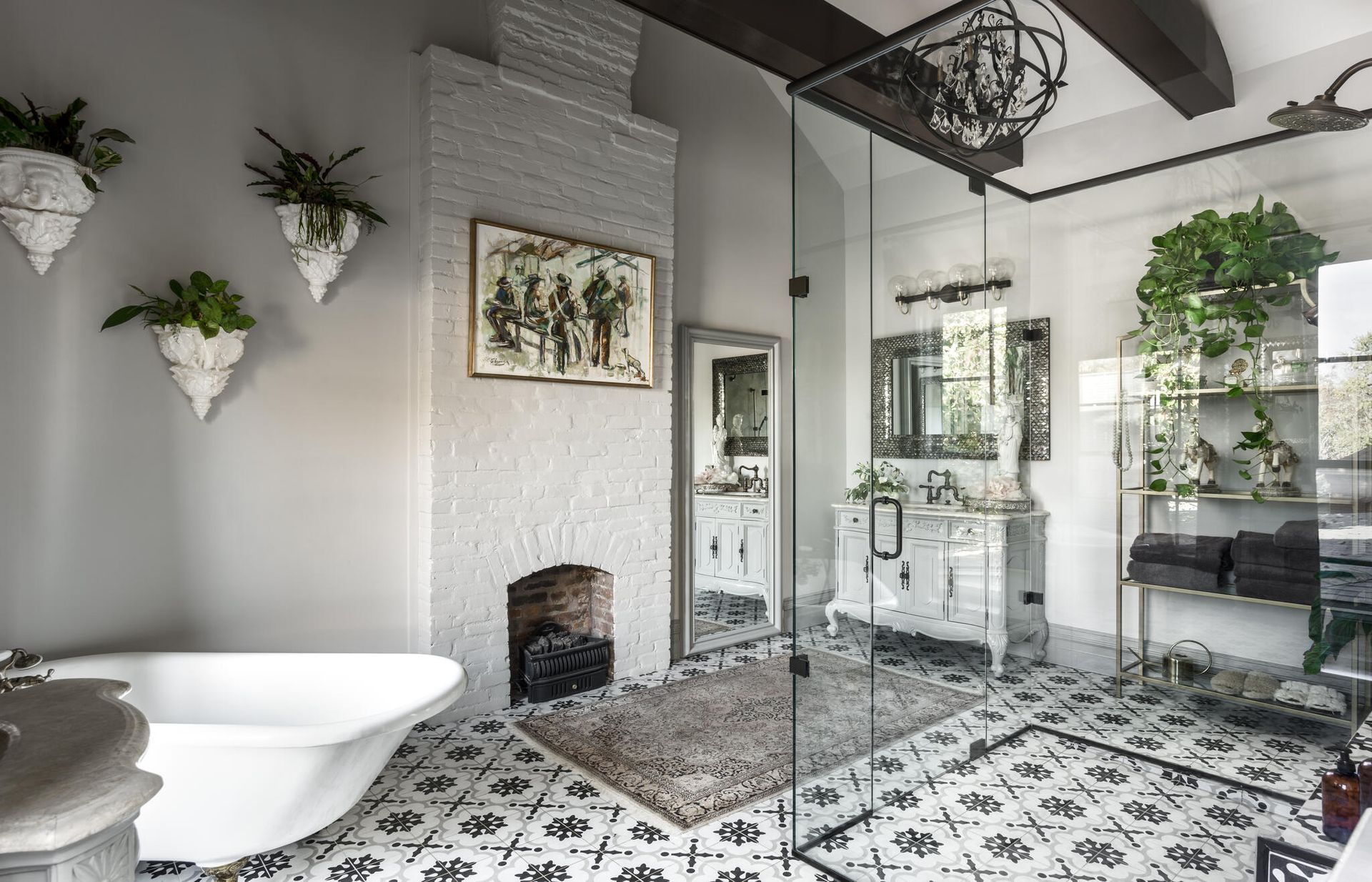 Renovated bathroom with a clawfoot tub, patterned encaustic tile floor, glass shower enclosure and a white painted brick fireplace